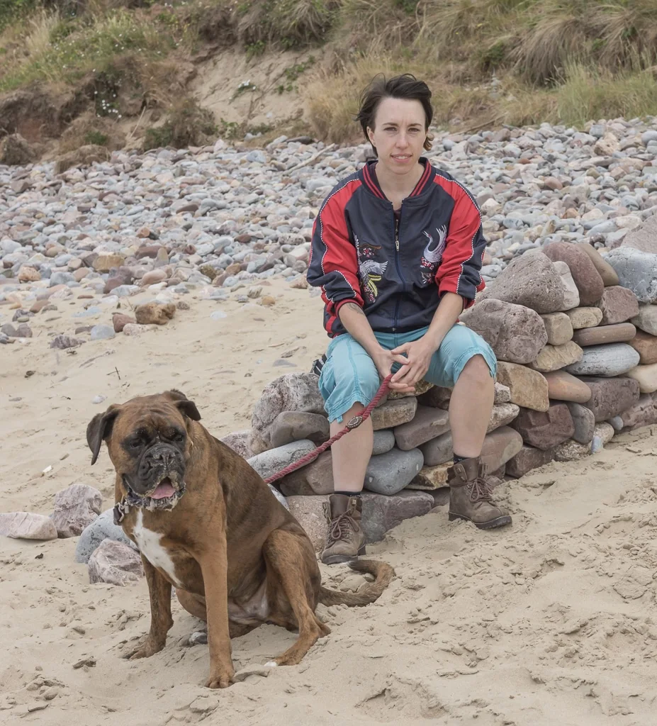 Jo sitting with a boxer dog on a beach
